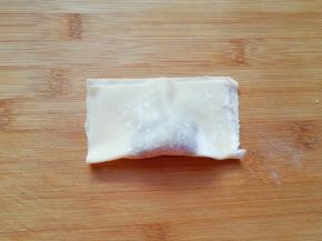 取一个馄饨皮放上肉馅，将馄饨皮对折，用两只手的大拇指和食指把有馅的地方捏挤一下，让馄饨馅团在一起。