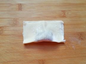 取一个馄饨皮放上肉馅，将馄饨皮对折，用两只手的大拇指和食指把有馅的地方捏挤一下，让馄饨馅团在一起。