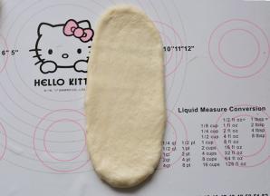 松弛好的面团进行排气、滚圆，用手轻轻滚成长条状，用擀面杖从中间上下擀开

，成牛舌状。