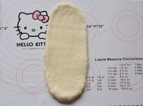 松弛好的面团进行排气、滚圆，用手轻轻滚成长条状，用擀面杖从中间上下擀开

，成牛舌状。