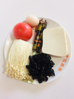 准备好所需的食材：

嫩豆腐1块，火腿肠2根，西红柿1个，鸡蛋1个，木耳提前泡发好，金针菇200克。