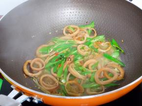 倒入鱿鱼圈大火爆炒，加点生抽、辣椒，炒至六成熟，把切好的青辣椒加入。辣椒提前洗净切好。