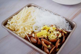 先把花甲放入烤盘中，放入蒜末和姜丝，再加入金针菇和粉丝