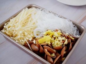 先把花甲放入烤盘中，放入蒜末和姜丝，再加入金针菇和粉丝