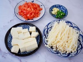 番茄先在顶部切十字，用开水烫至皮开，撕去皮切成小块，嫩豆腐切小块，金针菇去根部洗净备用，蒜切末，葱切葱花