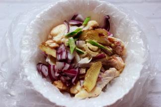 取一个大碗，碗里放入一个塑料袋，把鸡根放入塑料袋，加葱、姜、洋葱、胡椒粉、料酒。