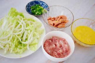 猪肉洗净切成薄片，加入料酒、盐、淀粉抓匀腌制备用，火腿肠切成片，鸡蛋打散备用，白菜洗净切成丝，葱切葱花