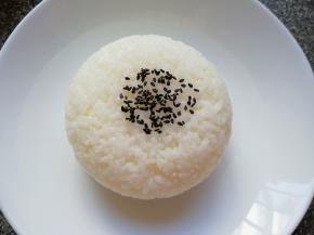 将蒸好的米饭盛在小碗里压实，然后倒扣在盘子里，撒上一些黑芝麻。