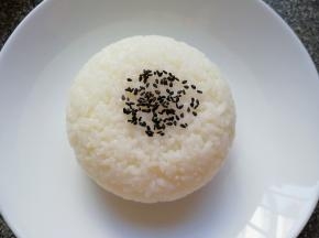 将蒸好的米饭盛在小碗里压实，然后倒扣在盘子里，撒上一些黑芝麻。