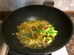 放入酸菜、蒜苗头、泡姜和泡椒翻炒2分钟。