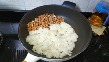 将午餐肉鲜菇丁推到锅的一边，倒入剩米饭，将饭压均匀后再和丁丁们炒均匀