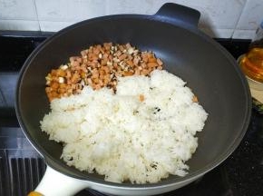 将午餐肉鲜菇丁推到锅的一边，倒入剩米饭，将饭压均匀后再和丁丁们炒均匀