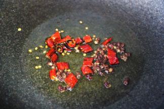 锅烧热后倒入花生油烧至六成热时，先爆香花椒和干辣椒。