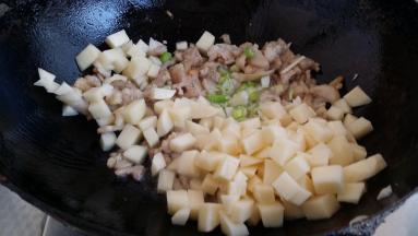 锅里放油下肉丁、土豆丁、蒜、葱一起煸炒变色烹入料酒。