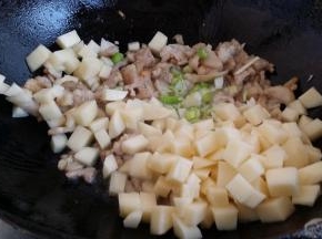 锅里放油下肉丁、土豆丁、蒜、葱一起煸炒变色烹入料酒。