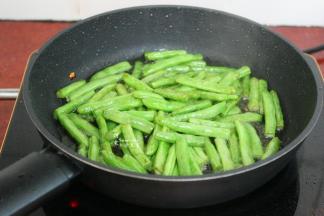 锅中有猪油，如果油少，可以适量的加点食用油，倒入四季豆大火干煸至四季豆有蔫菜的感觉，外皮皱皱的，微黄。