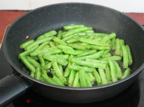锅中有猪油，如果油少，可以适量的加点食用油，倒入四季豆大火干煸至四季豆有蔫菜的感觉，外皮皱皱的，微黄。