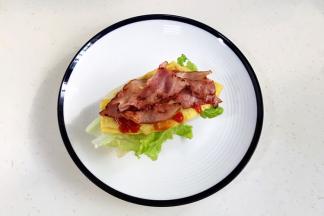 然后放入培根，接着继续放上煎蛋和生菜，挤上番茄酱，放上另一块飞饼即可。