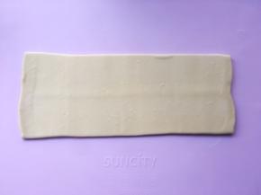 揉面垫上撒点干粉，将包裹好的面片收口朝下，用擀面杖轻轻擀成长条  