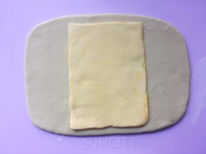 冰箱取出冷冻的黄油片，用剪刀裁开保鲜袋，将黄油片放在面片中间 