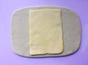 冰箱取出冷冻的黄油片，用剪刀裁开保鲜袋，将黄油片放在面片中间 