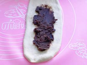 取一块面团，用擀面杖擀开，将气泡拍破。放上豆沙馅，抹平。将擀好的长舌状两边向中间对折，用擀面杖轻轻擀长。