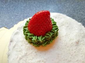 两颗草莓洗干净擦干水分，选一个“瘦高型”的草莓，削平底部，固定在蛋糕的一边，用绿色的奶油裱出圣诞树，如图。