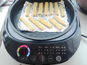 将电饼铛选择披萨功能，火力选择为中档，上下盘都进行加热，提前进行预热，将其底盘放上锡纸，将发酵好的奶棒条面包胚条，依次摆放好，放在锡纸上，如图所示。