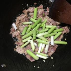 下入肉片翻炒变色，下入蒜苗茎部不停翻炒。