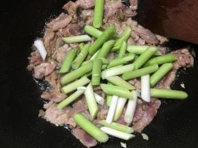 下入肉片翻炒变色，下入蒜苗茎部不停翻炒。