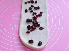 取一块面团，用擀面杖擀开，将气泡拍破，再放入蔓越莓干，将擀好的长舌状两边向中间对折，用擀面杖轻轻擀长，由上而下卷起。