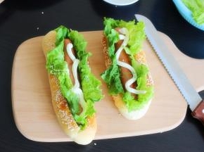接着放入煎好的牛肉肠，再挤一些沙拉酱在牛肉肠上，热狗面包就做好了。