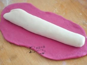 面醒好后，玫红色的面团擀开，将白色面团揉成管状，放在玫红色的面团上面。