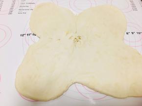 5、取出冷藏后的面团，依十字位置，将4个角向外侧按压后，用擀面杖向四个方面擀开，中间微微凸起