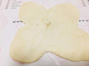 5、取出冷藏后的面团，依十字位置，将4个角向外侧按压后，用擀面杖向四个方面擀开，中间微微凸起