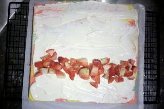 凉透的蛋糕脱模，底部垫油纸，把底部向下一会卷在外边哈，抹一层打发的淡奶油，放入草莓丁