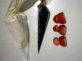 把余下的淡奶油装入裱花袋，准备巧克力膏，把草莓如图切去底部，切下顶部