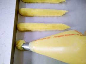 12将面糊装入裱花袋，用三能中号18齿裱花嘴，在烤盘里挤出长约10cm的长条，每个泡芙间隔要有2-3cm的空隙，防止泡芙膨胀粘连，表面喷水，用手将泡芙尾部尖角压平。