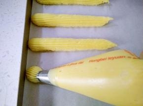 12将面糊装入裱花袋，用三能中号18齿裱花嘴，在烤盘里挤出长约10cm的长条，每个泡芙间隔要有2-3cm的空隙，防止泡芙膨胀粘连，表面喷水，用手将泡芙尾部尖角压平。