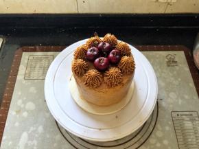 22、将剩余的咖啡奶油霜装入裱花袋里，裱花袋里提前装入齿形裱花嘴，在蛋糕表面挤上花型，中间放入车厘子装饰一下即可。