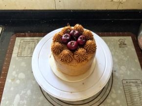 22、将剩余的咖啡奶油霜装入裱花袋里，裱花袋里提前装入齿形裱花嘴，在蛋糕表面挤上花型，中间放入车厘子装饰一下即可。