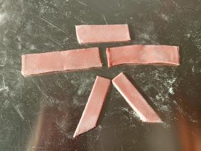 适量白色面团加红曲粉揉成红色面团，擀薄片，切宽条