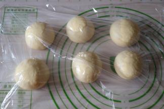 选择揉面程序揉面3分钟左右排气，然后分割成六等份一一揉圆，盖上保鲜膜静置松弛15分钟；
