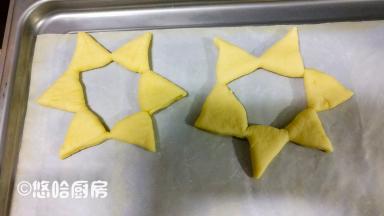 在面团上压出痕迹的地方，用刮板从面团中心依次切开，但是都不要切断，将所有的切口全部展开，衔接的地方稍微捏一下，避免散开。这个操作最好是在烤盘上进行，在案板上整形操作好了，移到烤盘上的时候，极为容易散开。依次做完全部面团，面团之间留有空隙，摆放在烤盘上。2份20克的面团，擀开后压出五角星的形状，用刮板切出五角星待用。