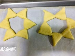 在面团上压出痕迹的地方，用刮板从面团中心依次切开，但是都不要切断，将所有的切口全部展开，衔接的地方稍微捏一下，避免散开。这个操作最好是在烤盘上进行，在案板上整形操作好了，移到烤盘上的时候，极为容易散开。依次做完全部面团，面团之间留有空隙，摆放在烤盘上。2份20克的面团，擀开后压出五角星的形状，用刮板切出五角星待用。
