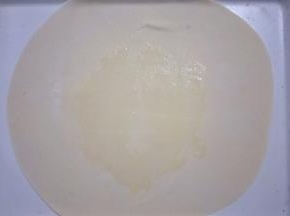 把略大的面团擀成厚度为1mm的薄饼，在饼中间刷一层油，然后撒上适量干面粉
