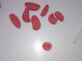 取一个小红色面团搓圆按扁，用纸棒戳两个小孔做成猪鼻子的形状