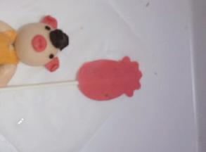 把红色旗子粘少量清水粘在纸棒上，放在小猪的右手臂处。把做好的帽子粘在小猪头顶部位。