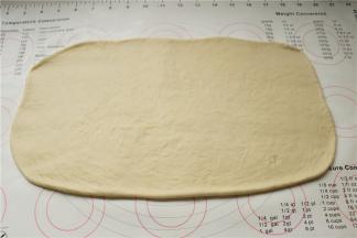 发酵好的面团移到揉面垫上，轻拍排出面团里面的气体，再擀成长方形片状。