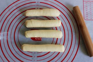 把椭圆形面皮从上往下卷起，卷面的时候要贴紧，往里面收，卷好之后，收口朝下。这是四个都卷好的热狗面包胚。